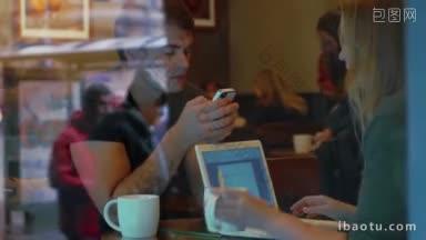 年轻人在咖啡馆的茶歇时间忙于他们的设备，男人用智能手机，女人在笔记本电脑上打字